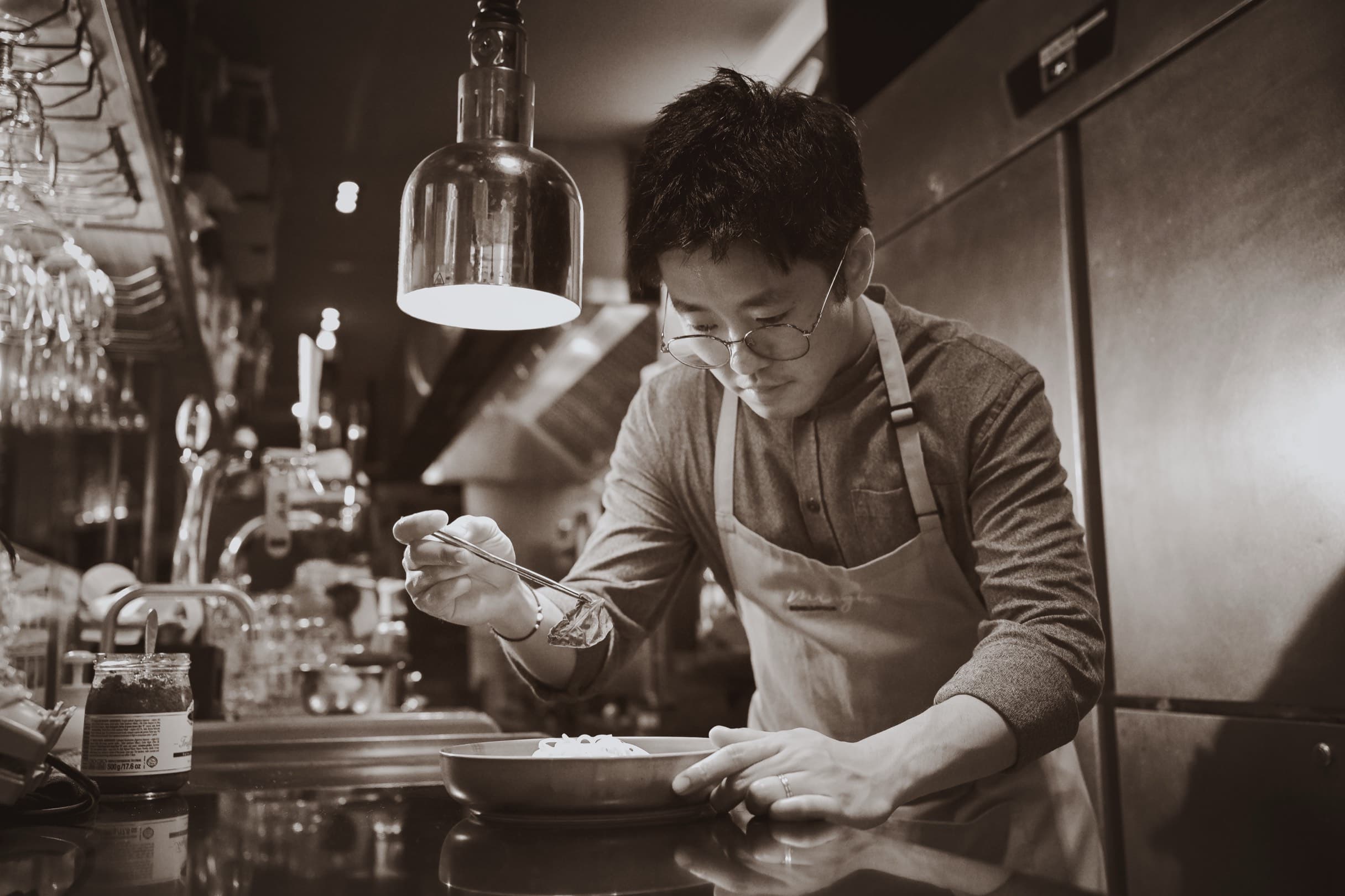 Dominic Yu plating a dish under the heat lamp at the pass