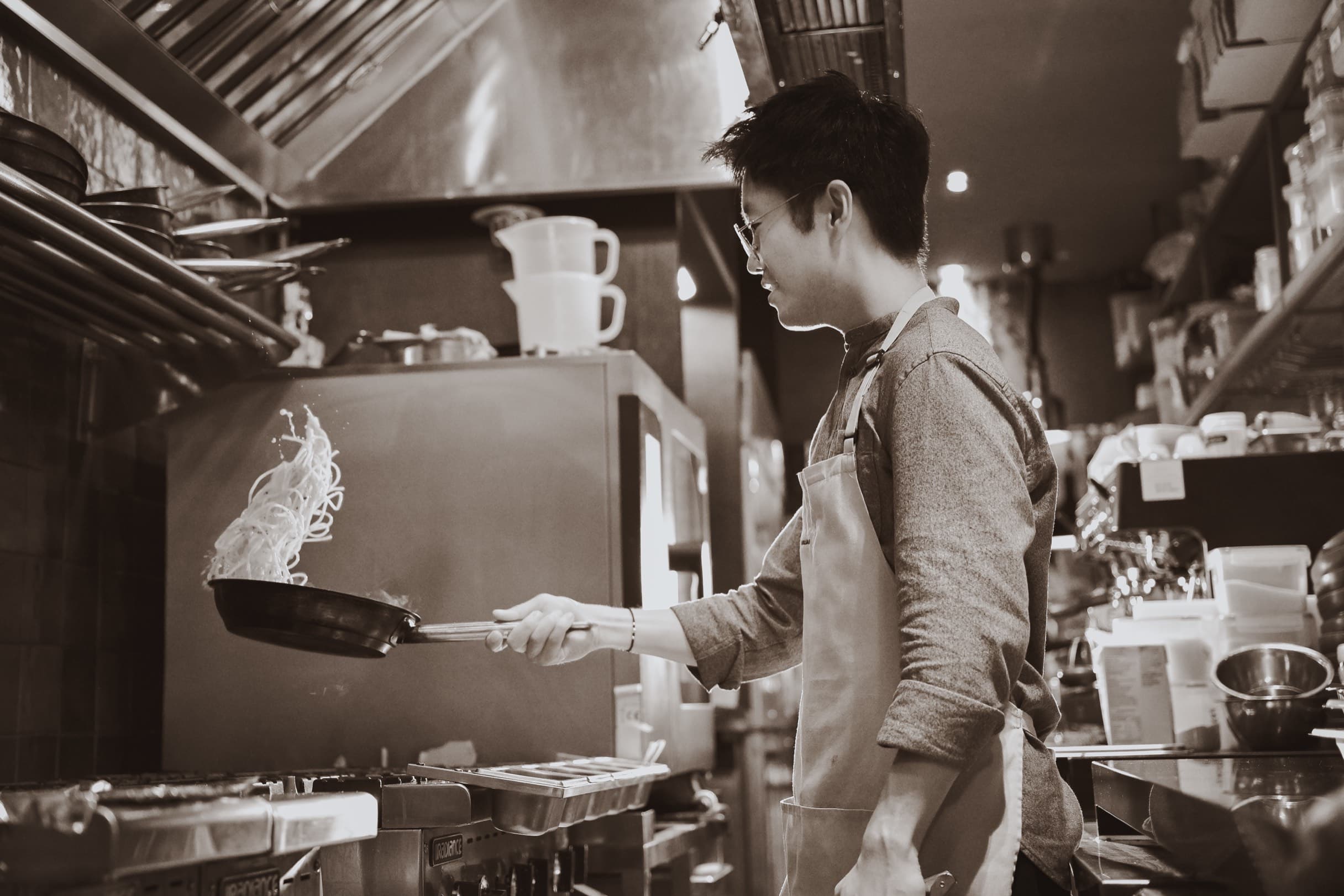 Dominic Yu tossing noodles in a pan on the line, mid-service